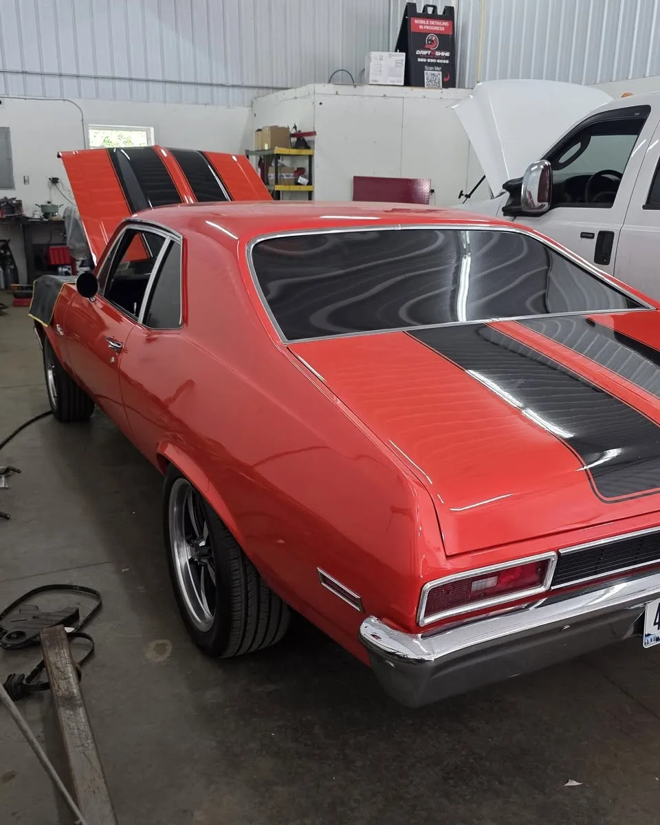 The back of a red Chevy Nova with black stripes, in the bay