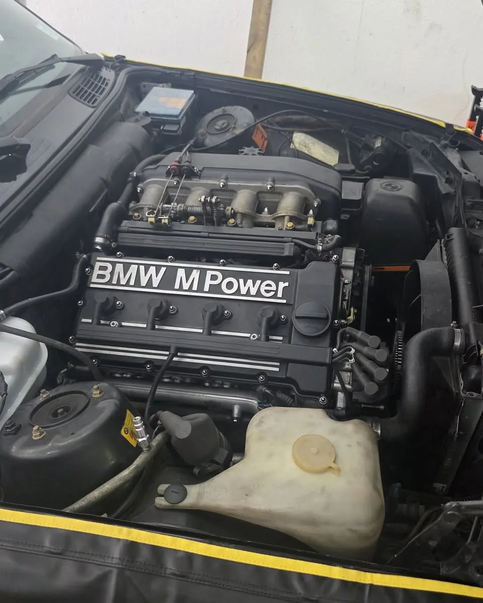 The BMW M Power engine of an E30 M3, under a fender cover
